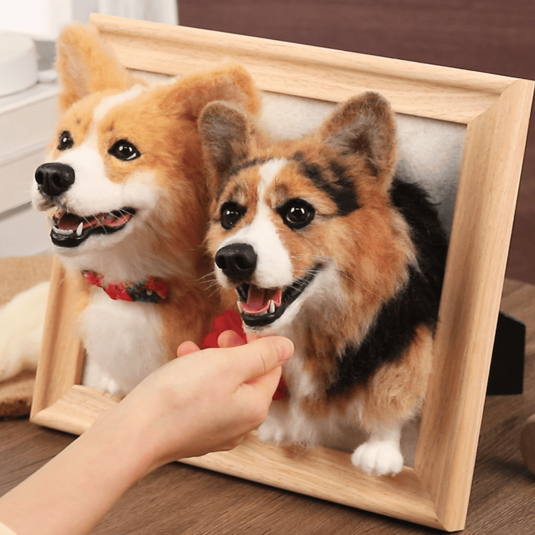 At_the_center_of_the_image_a_light-colored_wooden_frame_contains_two_lifelike_3D_felted_Corgi_portraits